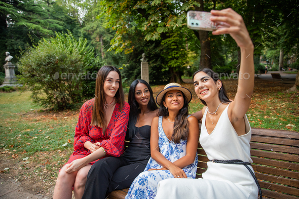Four friends are sitting on a patch in a public park and taking a selfie together. Diversity concep