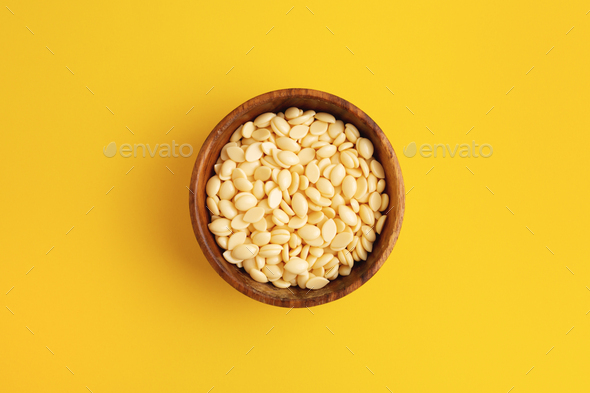 Film wax granules in a wooden bowl on yellow background.