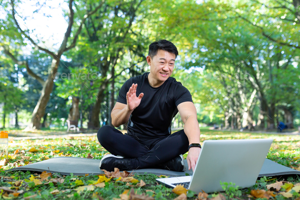 Fitness instructor works out online uses laptop in park sitting in lotus position