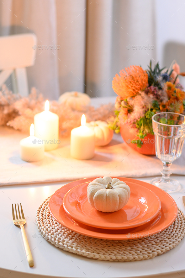 Thanksgiving day table setting with centerpiece of colorful flowers in pumpkin as vase.