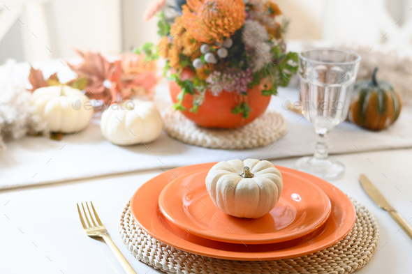 Thanksgiving day table setting with fall decorations of colorful flowers in pumpkin as vase.