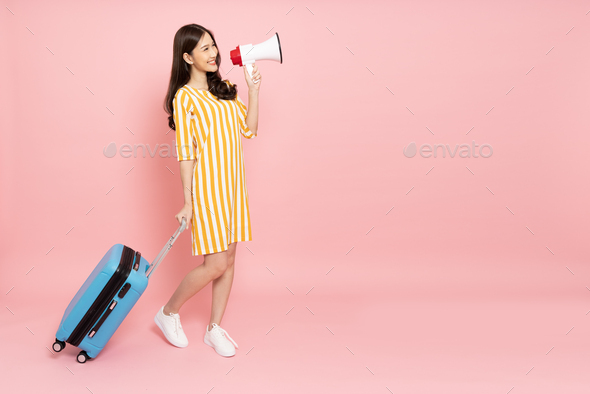 Happy young Asian woman traveler drag luggage and holding megaphone isolated on pink background
