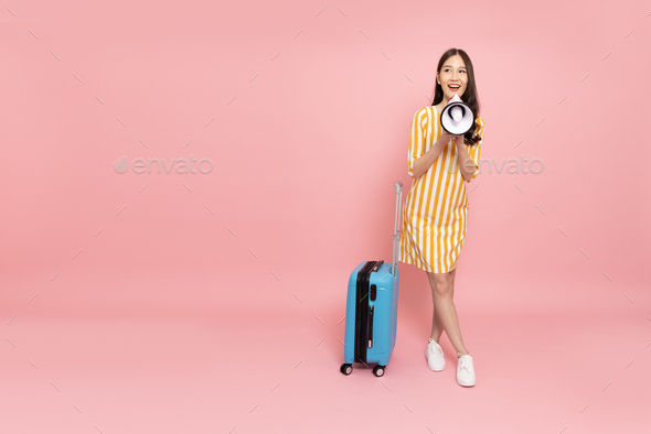 Happy young Asian woman traveler drag luggage and holding megaphone isolated on pink background,