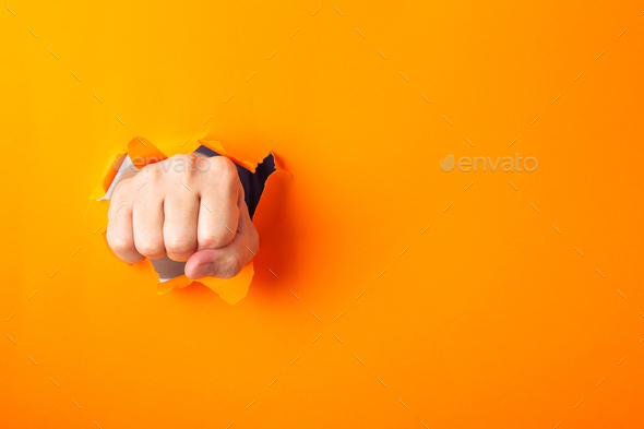Fist broke orange paper and torn a hole