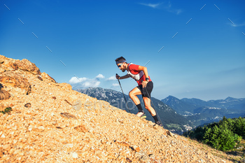 Young man uphill on rocky slope pushes with poles