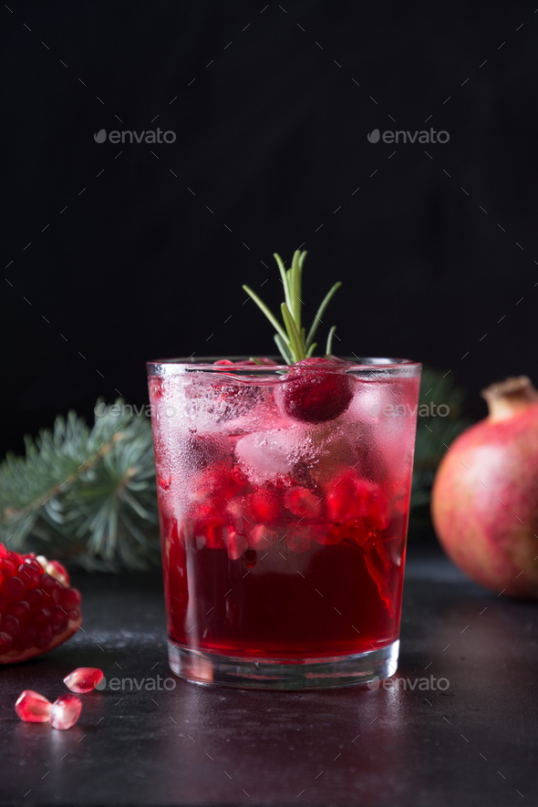 Pomegranate Christmas cocktail with rosemary, champagne, club soda on black table. Close up.