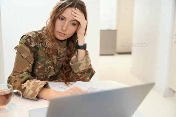 Woman liable for military service holds head with hand while working