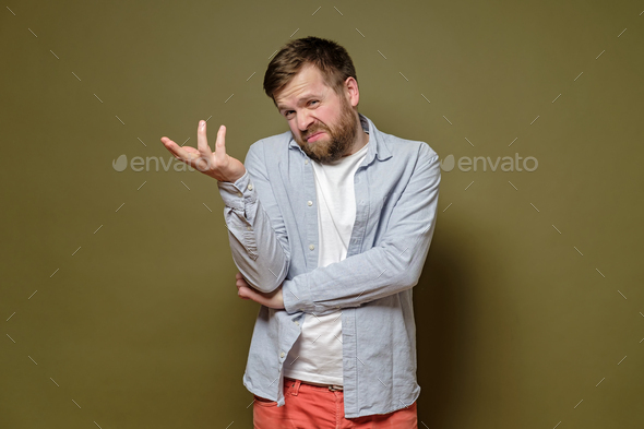 Caucasian man with a doubtful expression on face shrugs, makes a hand gesture and uncertain grimace