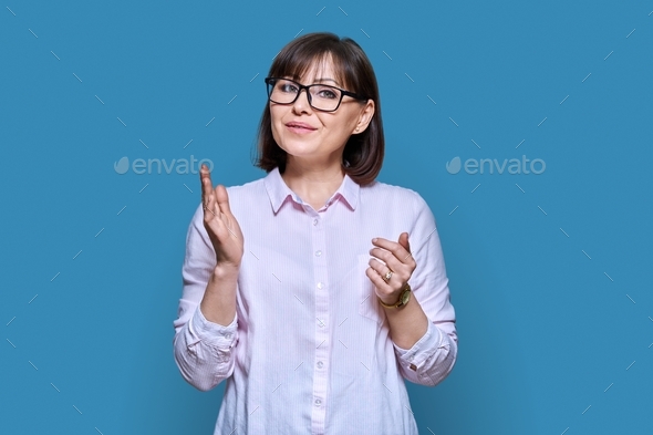 Talking gesturing woman looking at camera on blue studio background ...