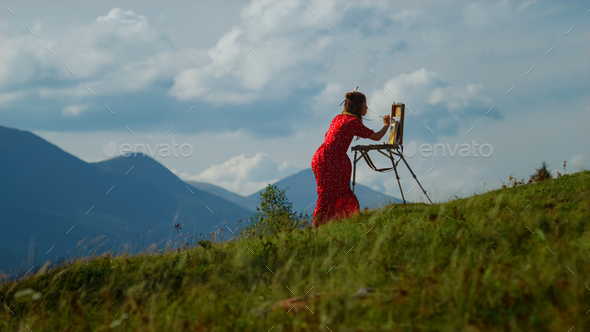 Creative girl painting mountains scenery outdoors. Woman drawing on nature.