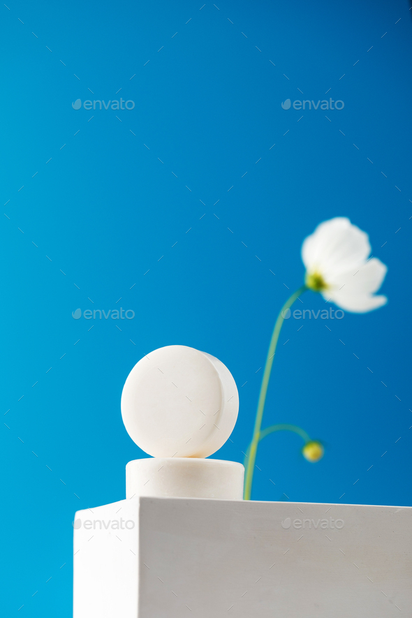 Round soap on a white podium on a blue background with a white flower.