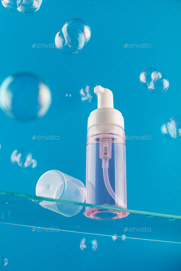 Dispenser mockup with face wash foam on a glass shelf with soap bubbles around. Skin care.