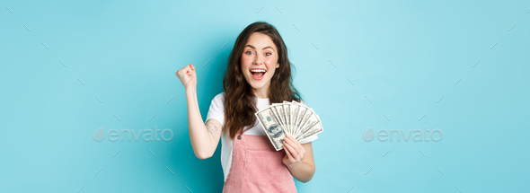 Excited smiling girl fist pump and hold money prize, winning cash, receive income from something