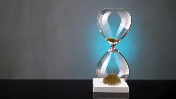 An Hourglass Made of Yellow Metal Shavings Passes Through a Funnel Symbolizing the Concept of Time