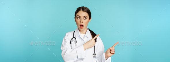 Surprised female doctor, physician with stethoscope, pointing and looking left with amazed, wow