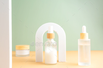 Beauty product concept. Jar of cream and bottles of serum on beige background in the arch. 