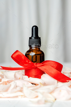 Vitamin serum in cosmetic bottle with rose flower petals on pink background. cosmetics aromatherapy.
