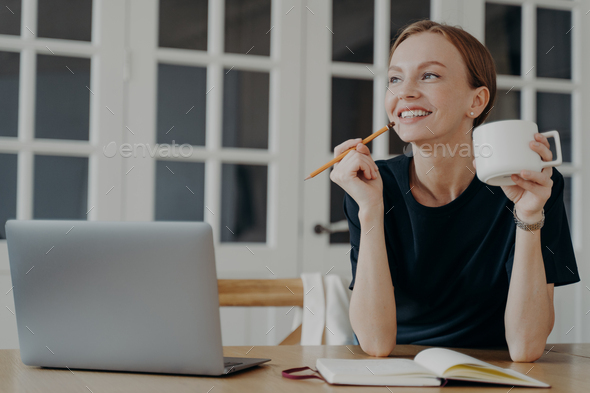 Smiling woman write notes in notebook, sitting at desk, thinking, planning day, visualizing dreams
