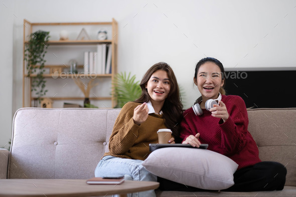 Two Young womanWatching TV Shaking Fists In Joy Celebrating Victory Of Favorite Sport Team Sitting