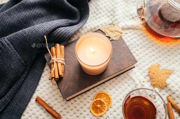Autumn mood, a burning candle, a book and a kettle of hot tea on a cozy plaid. Atmospheric mood