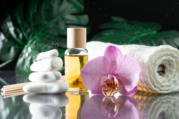 Lilac orchid flower, clear bottle of yellow oil, wooden sticks and towel with white stones and