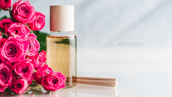 Bottle of yellow oil or perfume with wooden sticks and pink roses on white surface. SPA salon and
