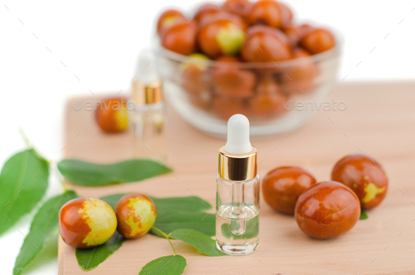 Jojoba oil in a transparent bottle with a dropper and fresh jojoba fruit on a wooden table