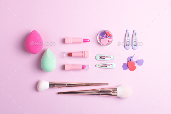 Girls makeup flat lay with various cosmetic products isolated on pink background.