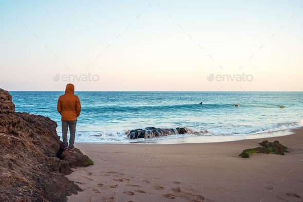 Man in a coat watches some guys surfing