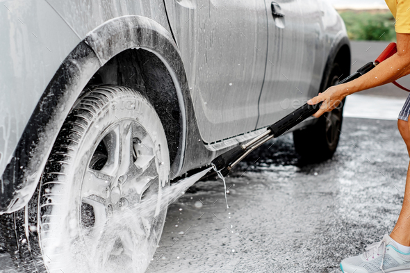 Close-up on woman holding high pressure pump washing her car in a self-service car wash station
