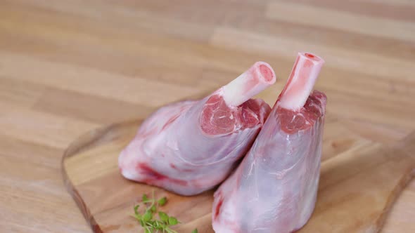 Pieces Of Fresh Uncooked Lamb Shank On A Wooden Chop Board Spinning. close up alt