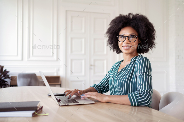 A woman with glasses works in an office typing a message to a client by mail.