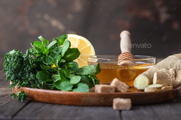 Mint, thyme, ginger root, lemon, honey and brown sugar on wooden plate.