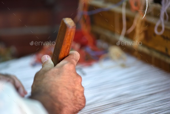 Unrecognizable master craftsman works on his loom by hand using a brush to make a traditional carpet