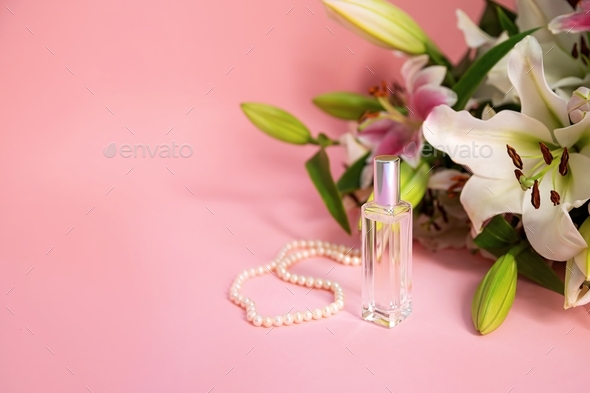 Women stuff: pearl neck chain, perfume and lilies on light pink background