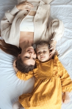 Top view happy family young mother and daughter lie together on bed and have fun at cozy home