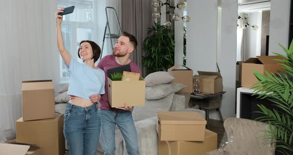 Young Couple Chatting with Friends or Family Online on Mobile Phone in New Apartment alt
