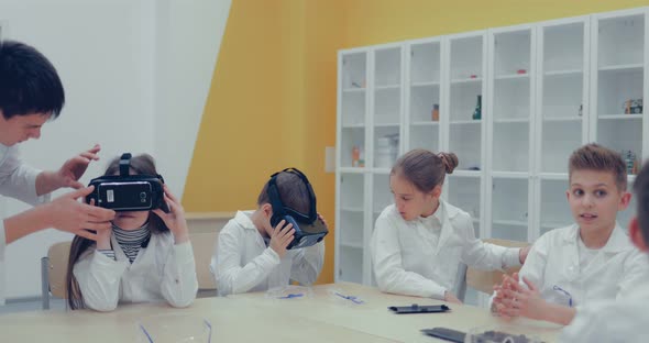 Schoolgirl and Schoolboy in the Classroom Watching in Virtual Reality Glasses alt