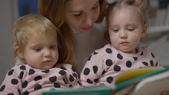 Closeup of Baby Twin Sisters Listening to Mother Reading Book in the Evening alt