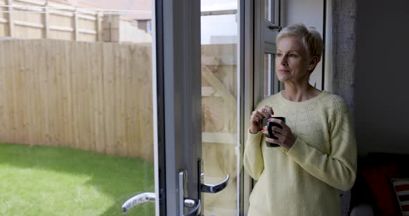 Mature woman stirring in coffee cup leaning on window