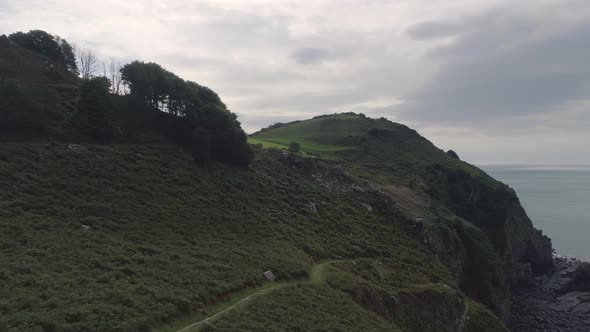 Low aerial tracking forward above the green grass above Wringcliff bay next to the valley of rocks, alt