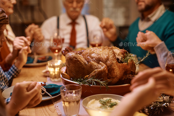 Thanksgiving turkey with family saying grace at dining table.