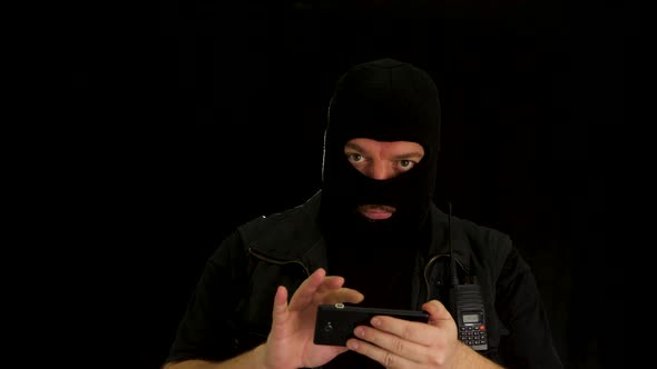 Concept idea: Computer hacker with balaclava manipulates cell phone and shows the result