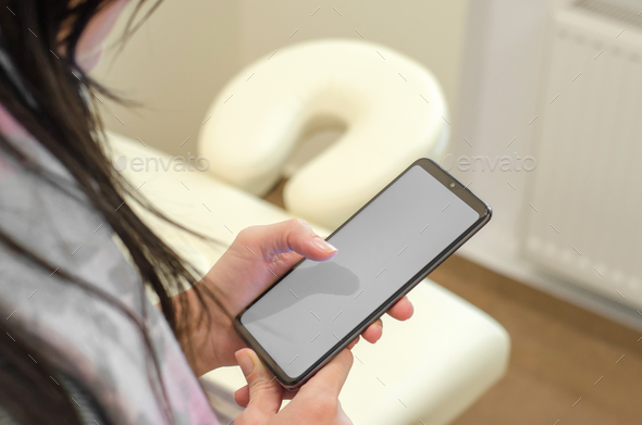 Phone with a blank white display in female hands on the background of a massage table