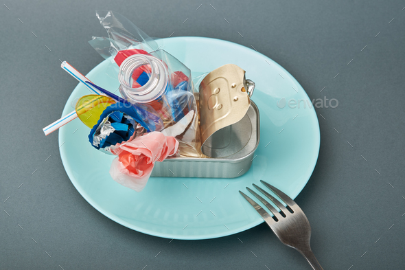 Open tin can on plate. Plastic waste instead of fish inside. Ocean plastic pollution concept