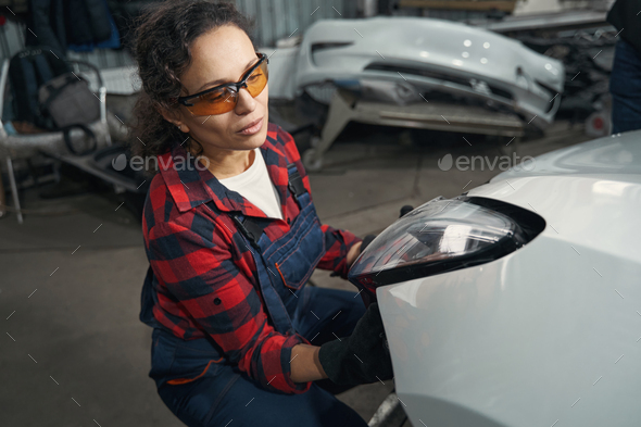 Female auto mechanic repairing car headlight in garage