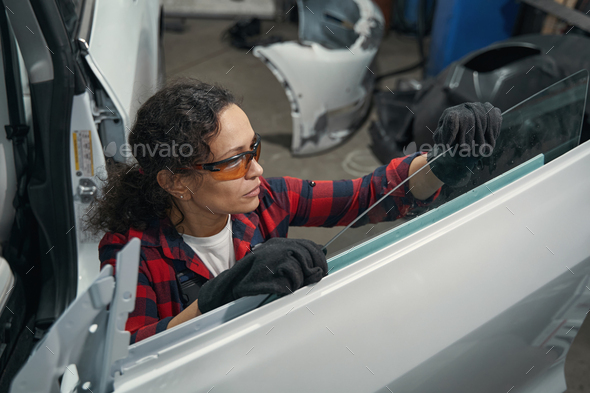 Female auto mechanic repairing vehicle door in garage