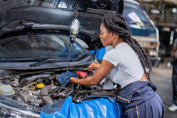 Mechanical girl at car repair shop stand pulling engine oil dipstick