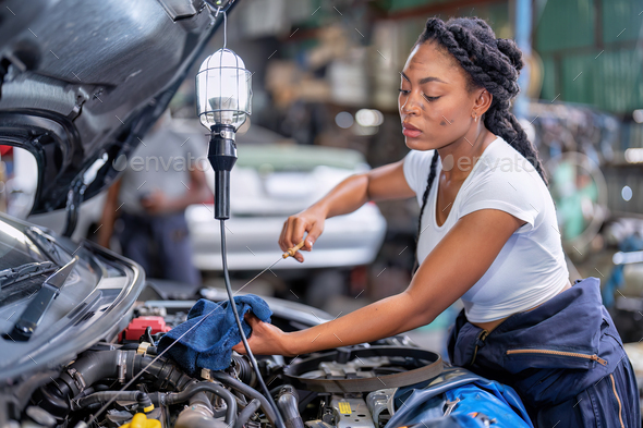Mechanical girl at car repair shop stand pulling engine oil dipstick