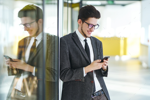Young office worker in glasses using mobile smart phone. Businessman holds telephone in hand.